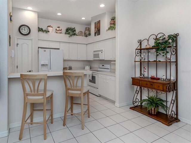 kitchen with kitchen peninsula, white appliances, white cabinets, and light tile patterned flooring