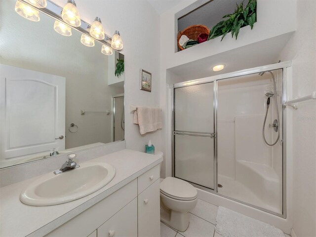 bathroom featuring a shower with door, vanity, toilet, and tile patterned flooring