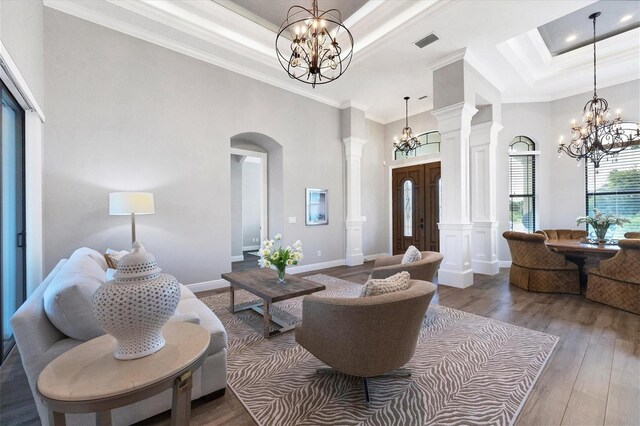 living room featuring wood-type flooring, a high ceiling, decorative columns, ornamental molding, and a chandelier