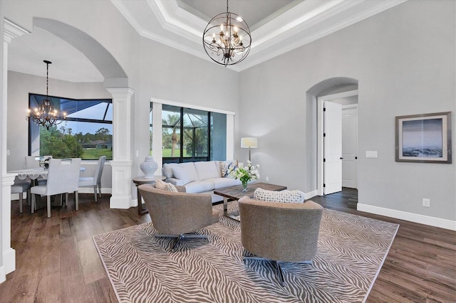 living room featuring a notable chandelier, decorative columns, dark wood-type flooring, and crown molding