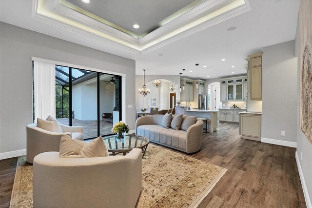 living room featuring ornamental molding, a raised ceiling, a chandelier, and dark hardwood / wood-style flooring