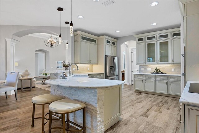 kitchen featuring backsplash, pendant lighting, light wood-type flooring, stainless steel fridge with ice dispenser, and a notable chandelier