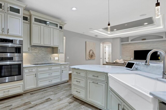 kitchen featuring a raised ceiling, black electric stovetop, double oven, and decorative light fixtures