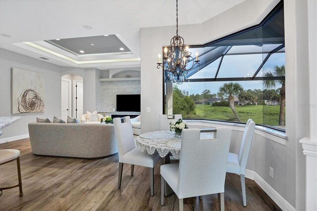 dining space with a chandelier, a tray ceiling, hardwood / wood-style flooring, and a fireplace