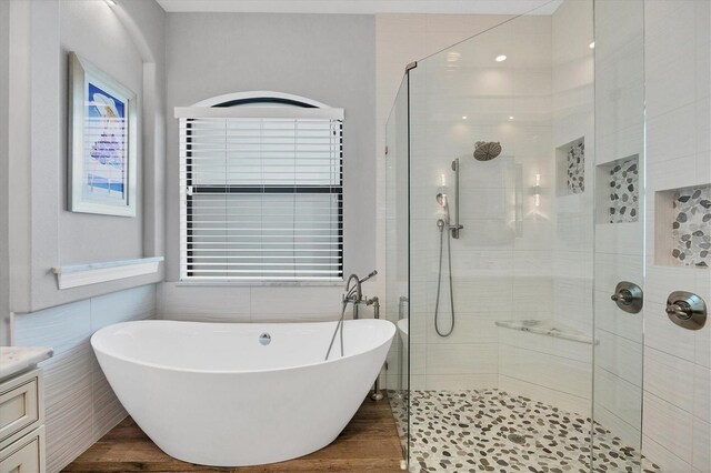 bathroom with independent shower and bath, vanity, tile walls, and wood-type flooring