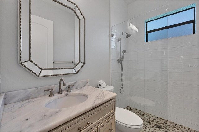 bathroom with a tile shower, vanity, and toilet