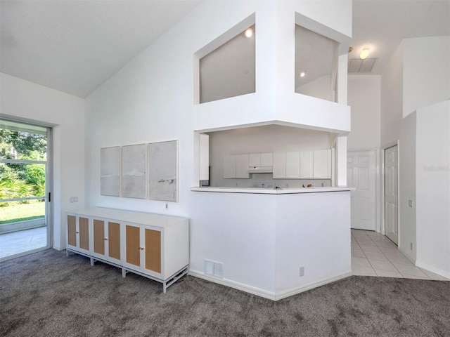 kitchen with kitchen peninsula, high vaulted ceiling, white cabinetry, and light colored carpet