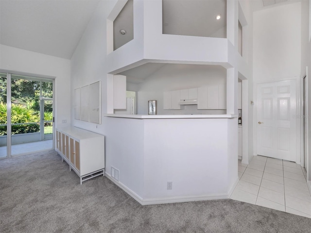 kitchen with white cabinetry, kitchen peninsula, high vaulted ceiling, and light carpet