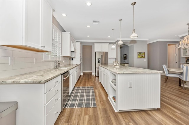 kitchen featuring sink, white cabinets, decorative light fixtures, a kitchen island, and appliances with stainless steel finishes