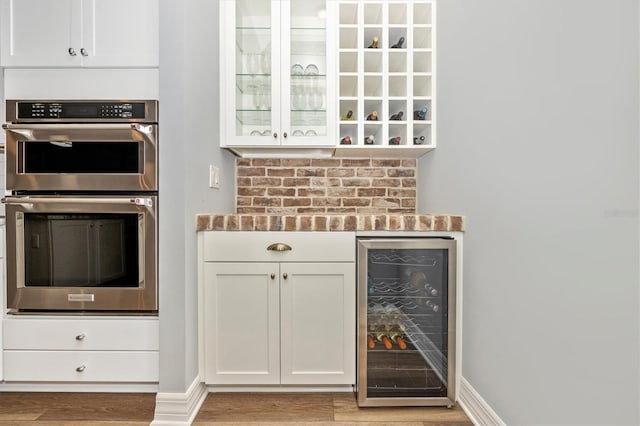 kitchen with white cabinets, stainless steel double oven, light hardwood / wood-style floors, and wine cooler