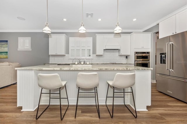 kitchen featuring light stone counters, stainless steel appliances, pendant lighting, white cabinets, and a kitchen island