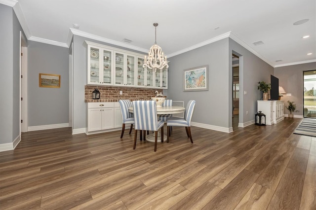 dining area featuring dark hardwood / wood-style floors, indoor bar, crown molding, and an inviting chandelier