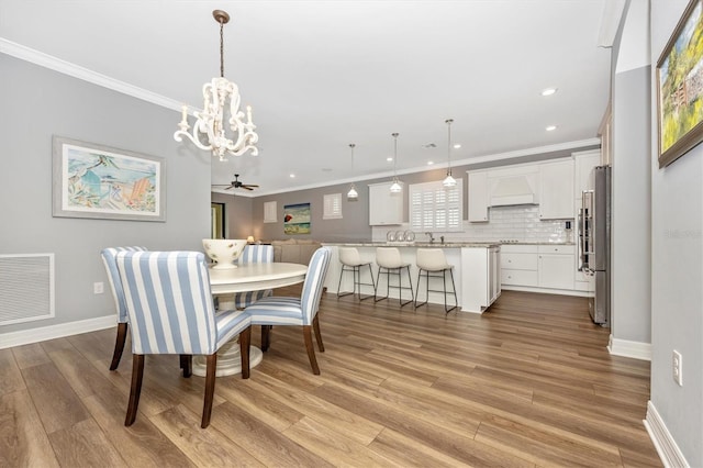 dining area featuring light wood-type flooring, ceiling fan with notable chandelier, crown molding, and sink