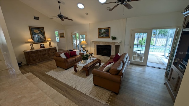 living room featuring high vaulted ceiling, ceiling fan, a tile fireplace, and light hardwood / wood-style flooring