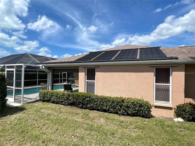 rear view of house featuring a lanai, a lawn, and solar panels