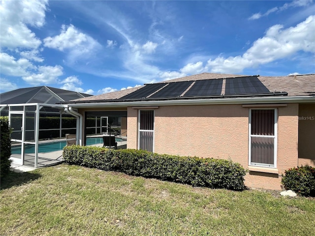 back of property featuring solar panels, a yard, an outdoor pool, stucco siding, and a lanai