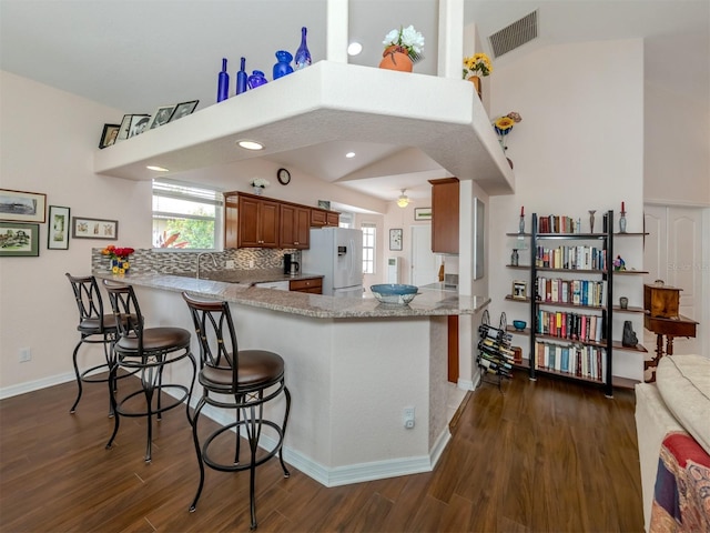 kitchen with white refrigerator with ice dispenser, tasteful backsplash, kitchen peninsula, light stone countertops, and dark wood-type flooring