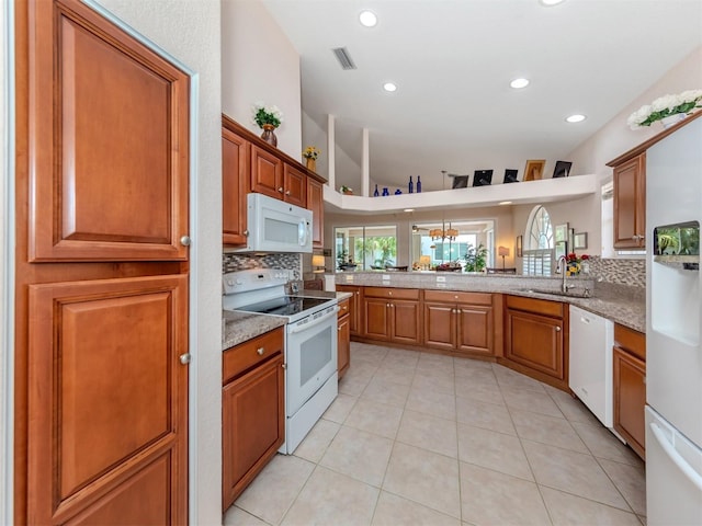 kitchen with white appliances, backsplash, kitchen peninsula, light stone counters, and light tile patterned flooring