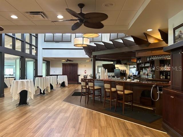 bar with ceiling fan and light hardwood / wood-style floors