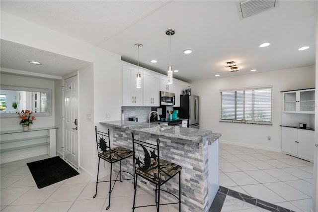 kitchen with kitchen peninsula, appliances with stainless steel finishes, light stone countertops, tasteful backsplash, and white cabinetry