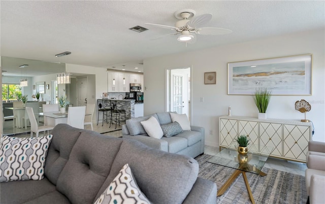 living room featuring ceiling fan, light tile patterned flooring, and a textured ceiling