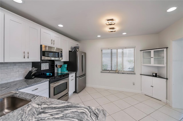 kitchen featuring light stone countertops, decorative backsplash, stainless steel appliances, light tile patterned floors, and white cabinetry