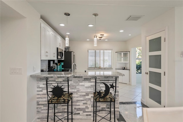 kitchen featuring white cabinets, light stone countertops, appliances with stainless steel finishes, a kitchen bar, and kitchen peninsula