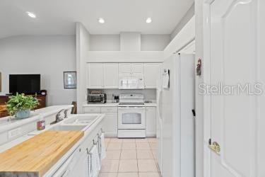 kitchen with light tile patterned floors, wood counters, white appliances, white cabinetry, and sink