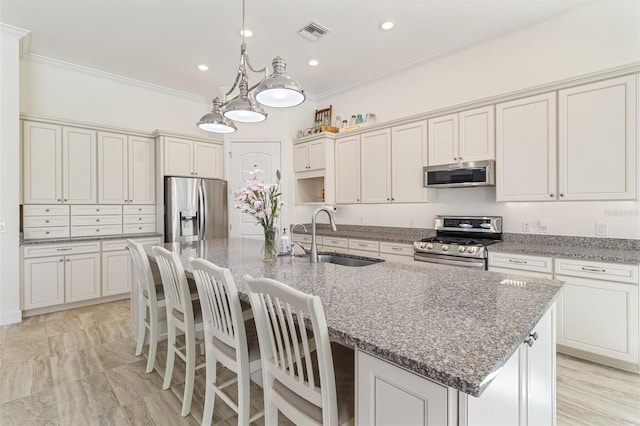 kitchen with a center island with sink, visible vents, appliances with stainless steel finishes, ornamental molding, and a sink