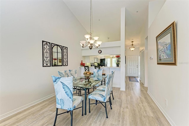 dining area with light wood-type flooring, an inviting chandelier, baseboards, and high vaulted ceiling