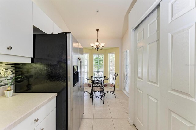 kitchen featuring stainless steel fridge, light tile patterned floors, white cabinetry, pendant lighting, and a notable chandelier