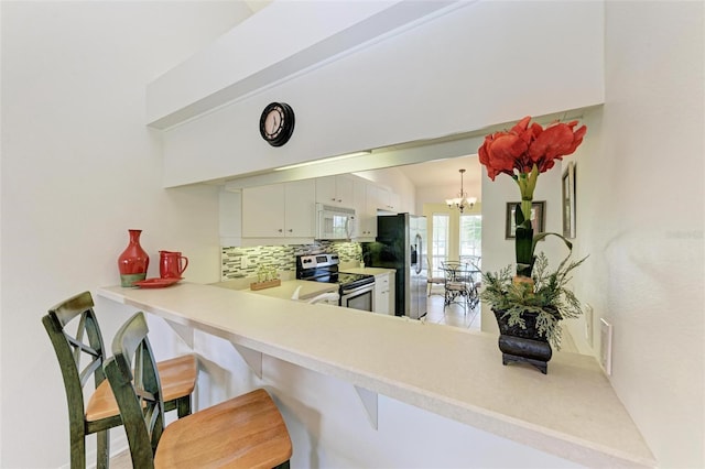 kitchen with a breakfast bar, light countertops, appliances with stainless steel finishes, tasteful backsplash, and an inviting chandelier