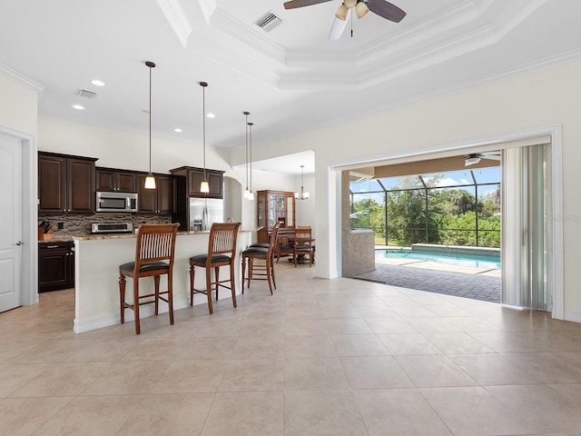 kitchen featuring a tray ceiling, stainless steel appliances, ceiling fan, and a breakfast bar