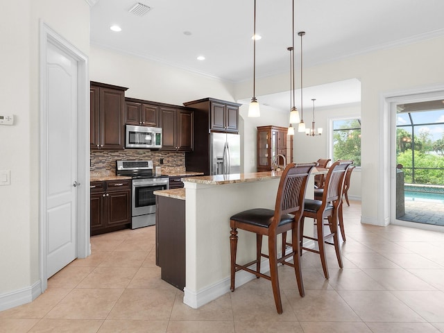 kitchen with light stone countertops, light tile patterned floors, appliances with stainless steel finishes, a kitchen island with sink, and decorative backsplash