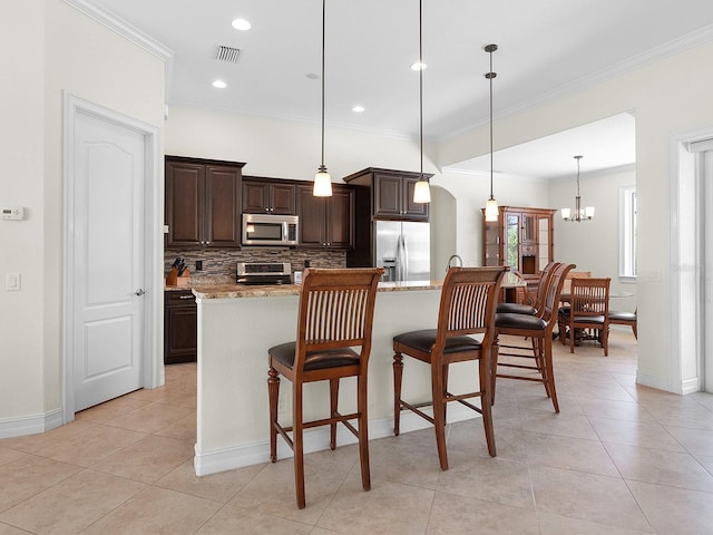 kitchen featuring backsplash, appliances with stainless steel finishes, hanging light fixtures, ornamental molding, and light stone counters