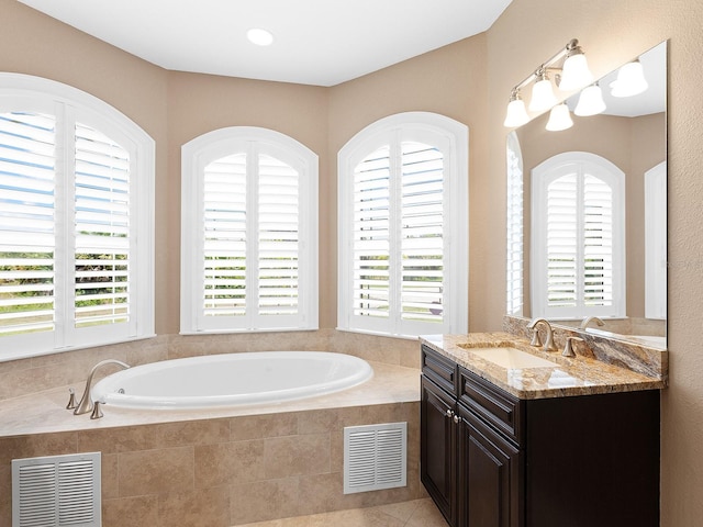 bathroom with a wealth of natural light, tiled bath, and vanity