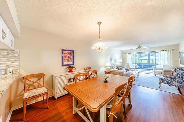 dining room featuring ceiling fan with notable chandelier, dark wood-type flooring, and a textured ceiling