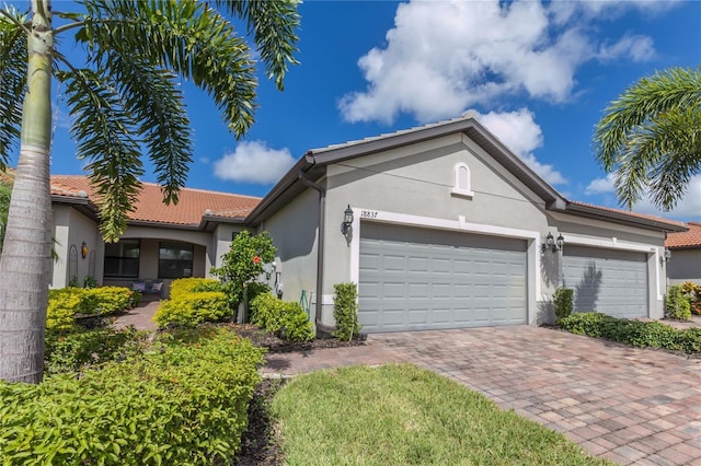 view of front facade with stucco siding, an attached garage, a tile roof, and decorative driveway