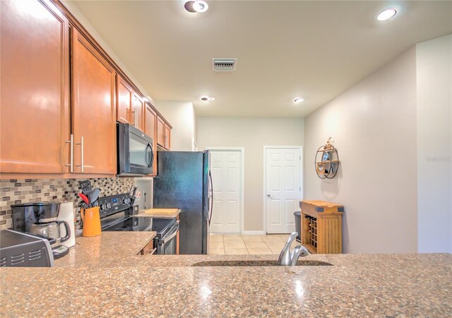 kitchen featuring visible vents, black appliances, a sink, tasteful backsplash, and brown cabinetry