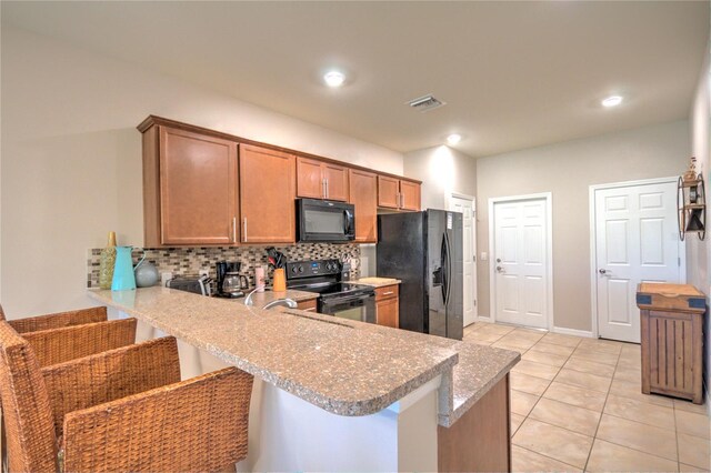 kitchen with visible vents, brown cabinets, a peninsula, black appliances, and tasteful backsplash