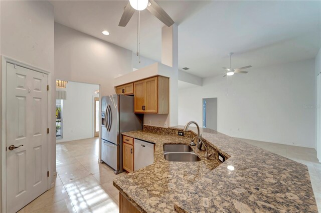 kitchen with stone counters, appliances with stainless steel finishes, a ceiling fan, a sink, and a peninsula