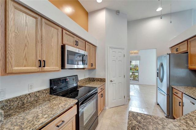 kitchen with a high ceiling, light stone counters, stainless steel appliances, and light tile patterned flooring