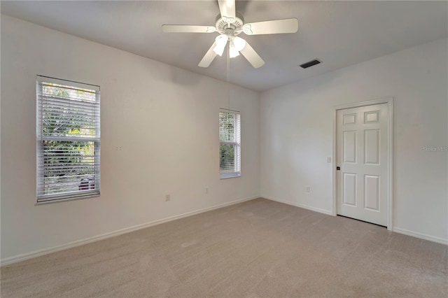 empty room with baseboards, visible vents, a ceiling fan, and light colored carpet