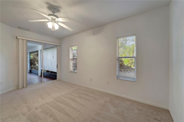 unfurnished room with a wealth of natural light, light colored carpet, visible vents, and baseboards