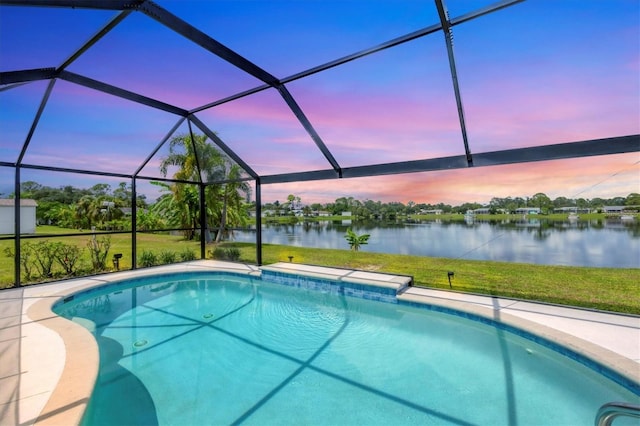 pool at dusk featuring a water view, a lawn, and a lanai