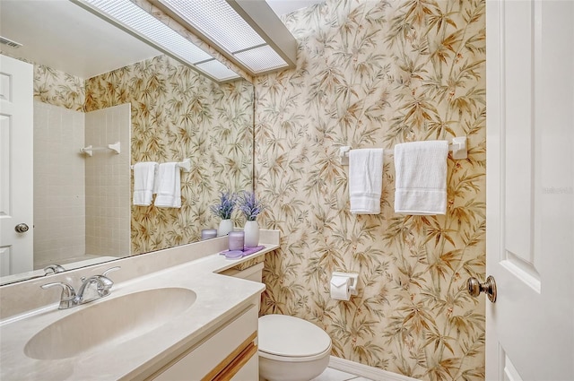 bathroom featuring baseboards, vanity, toilet, and wallpapered walls