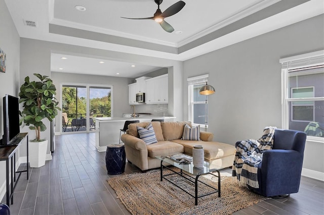 living room with dark wood-type flooring, a tray ceiling, ceiling fan, and ornamental molding