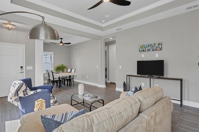 living room with crown molding, dark wood-type flooring, a raised ceiling, and ceiling fan