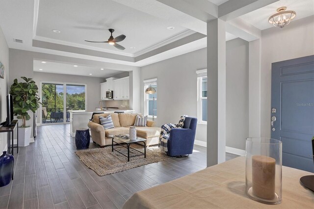 living room featuring a raised ceiling, sink, ceiling fan with notable chandelier, and dark hardwood / wood-style flooring