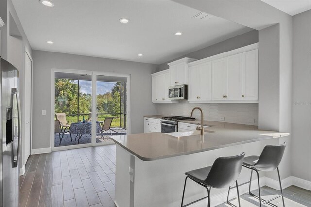 kitchen featuring white cabinetry, kitchen peninsula, stainless steel appliances, and light hardwood / wood-style floors